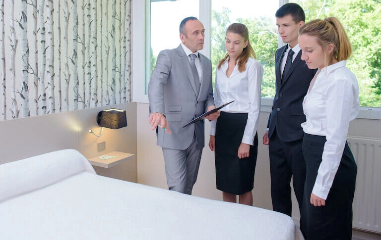 Two people wearing suits or hotel uniforms knock The Room Inspector Distraction